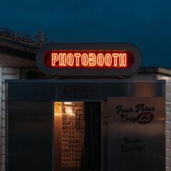 A neon-lit photobooth entrance captured against the night sky in Brighton, England.